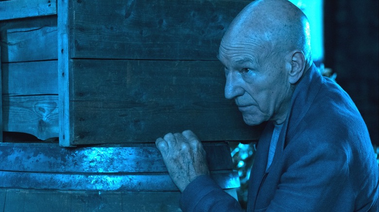 Admiral Picard in a blue, dark room, hiding by boxes in Star Trek: Picard