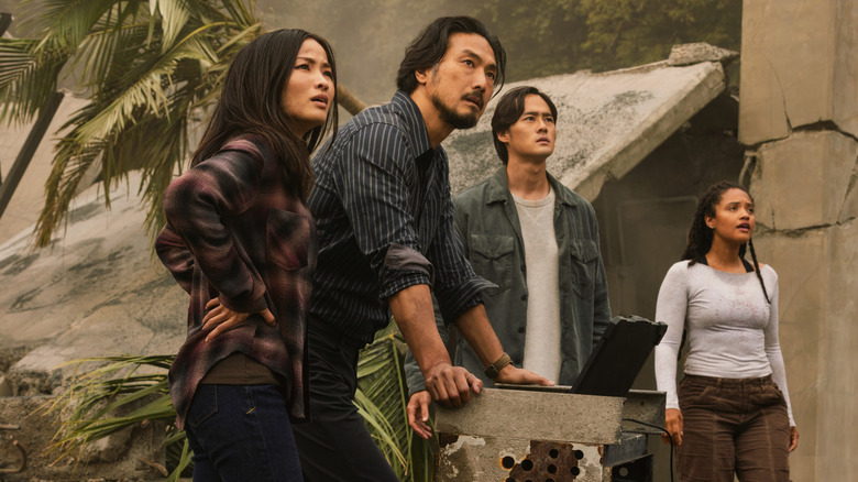 Anna Sawai as Cate, Takehiro Hira as Hiroshi, Ren Watabe as Kentaro, and Kiersey Clemons as May standing in a jungle by a laptop and looking into the distance in Monarch: Legacy of Monsters