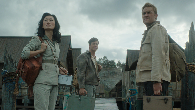 Mari Yamamoto as Keiko, Anders Holm as Bill, and Wyatt Russell as Lee wearing backpacks and looking over their shoulders in a small town in Monarch: Legacy of Monsters