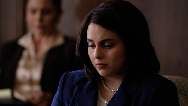 Monica looking down wearing a blue top and pearls in Impeachment: American Crime Story