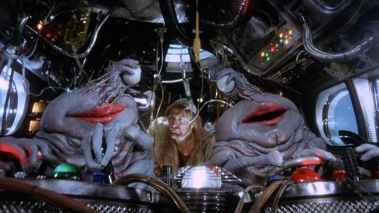 Aliens with large red lips and eyeballs held by hands on their head look at their stowaway, Brian (Graham Chapman), in Life of Brian