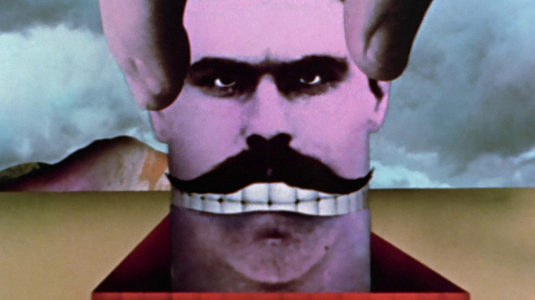 Un hombre con una cabeza en forma de tubo, sacado por una mano enorme, de una caja plana en el suelo, ambientado en un paisaje tipo Dalí, de Monty Python