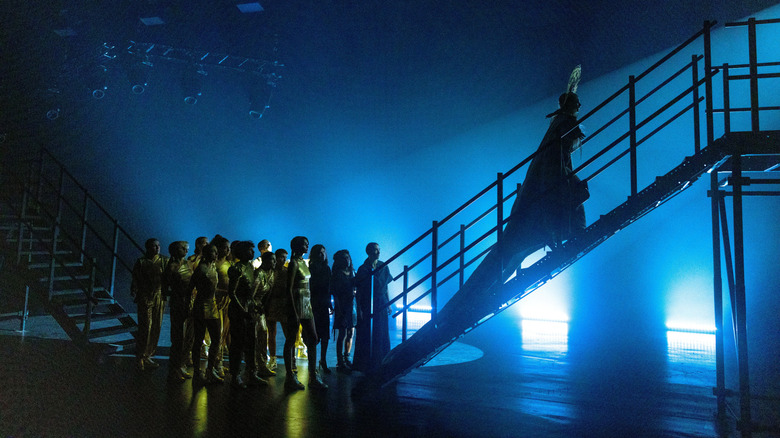 Mother Mary ascending up a staircase to a stage in Mother Mary while a crowd looks on