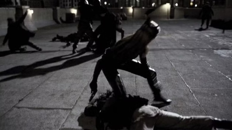 Catwoman (Anne Hathaway) looks behind her as Batman (Christian Bale) fights henchmen in The Dark Knight Rises