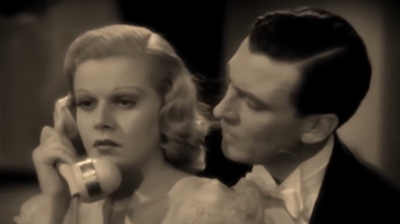 Carol (Jean Harlow) on telephone as Hartley (Walter Pidgeon) looks on in Saratoga