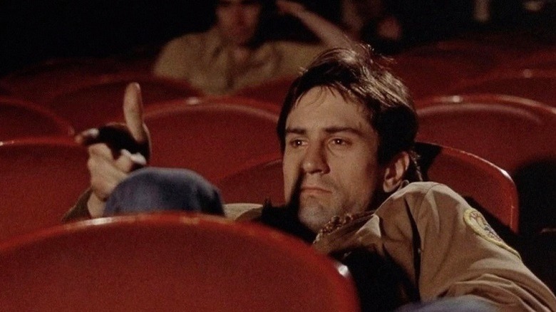 Travis Bickle sits in a half empty cinema, miming shooting at the screen