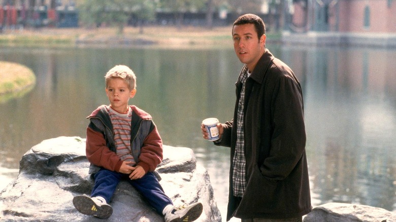 Adam Sandler stands  holding a cup beside one of the Sprouse twins  