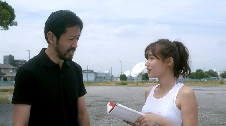 Takayuki Hamatsu as Takayuki Higurashi and Yuzuki Akiyama Aika Matsumoto in One Cut of the Dead, standing outside and talking over a script.