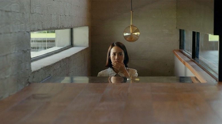 Cho Yeo-jeong as Choi Yeon-gyo in Parasite, walking up a set of stairs in a nice house and holding her hand over her mouth.