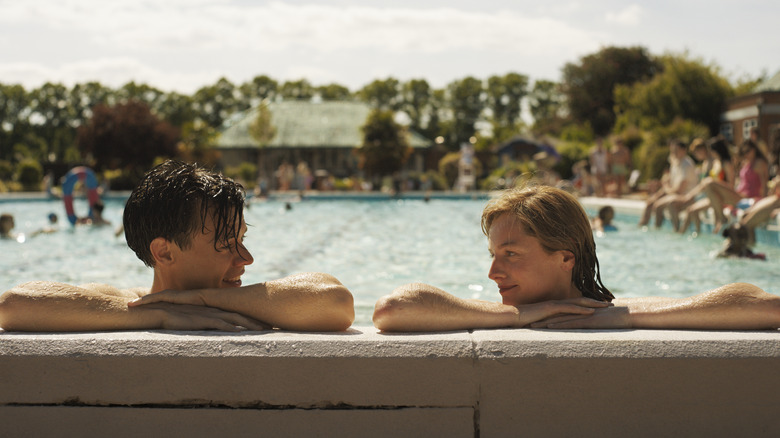 harry styles and emma corrin smiling at each other in a pool in the movie my policeman