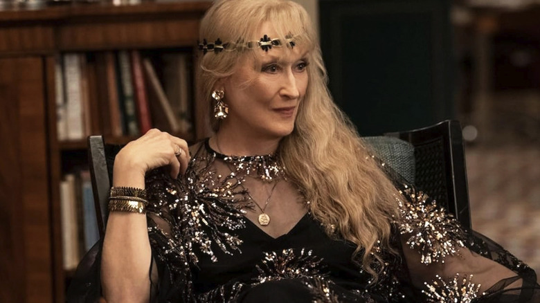 Loretta wearing ostentatious clothing and sitting in a chair in Only Murders in the Building