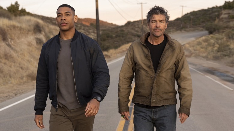 Aaron Pierre as John Stewart and Kyle Chandler as Hal Jordan walking down a dusty road in plainclothes in Lanterns