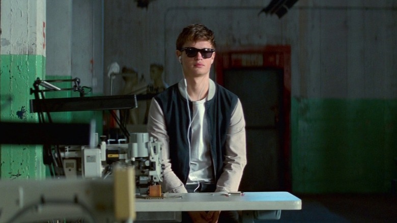 బేబీ డ్రైవర్‌లో బేబీగా అన్సెల్ ఎల్‌గార్ట్, గిడ్డంగిలో తన సన్‌గ్లాసెస్ మరియు ఇయర్‌బడ్స్ ధరించాడు