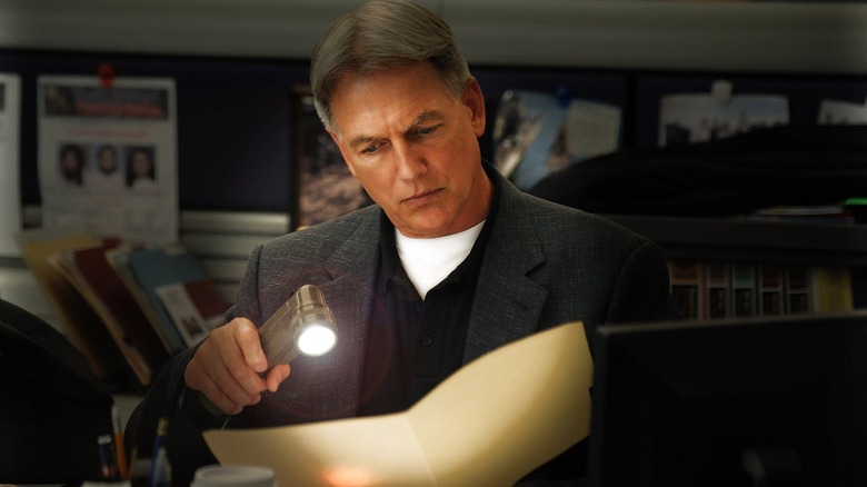 Mark Harmon as Leroy Jethro Gibbs, inspecting a file with a flashlight, in NCIS