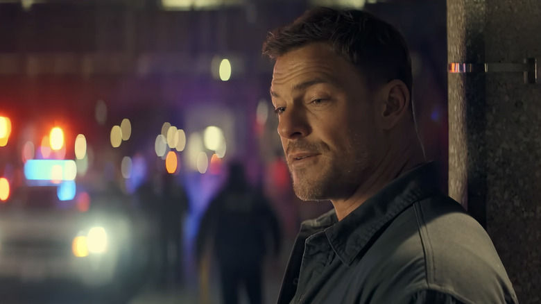 Alan Ritchson's Jack Reacher leans against a pole on a street in Neagley