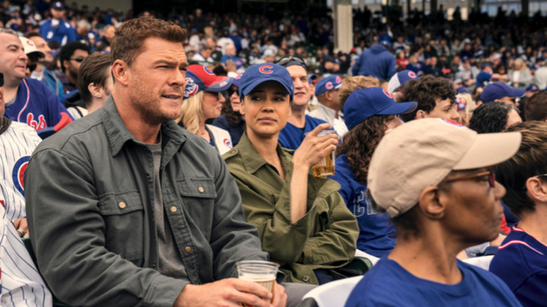 Alan Ritchson's Jack Reacher sits beside Maria Sten's Frances Neagley at a baseball game in Neagley