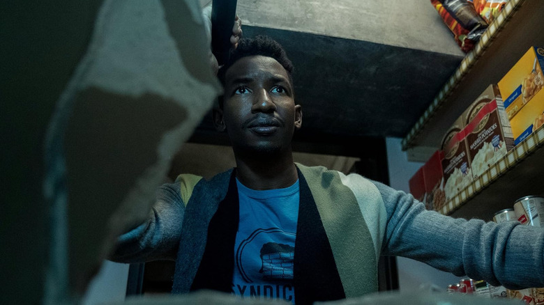 Dan (Mamoudou Athie) holding a flashlight while searching a closet full of food in 