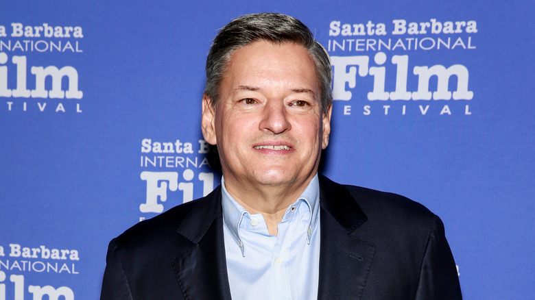man in a black jacket and blue shirt in front of a blue background that reads "santa barbara international film festival"