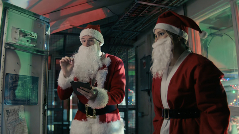 Olivia Holt's Sophie Arbus stands alongside Connor Swindell's Nick O'Connor as they both wear santa suits in Jingle Bell Heist