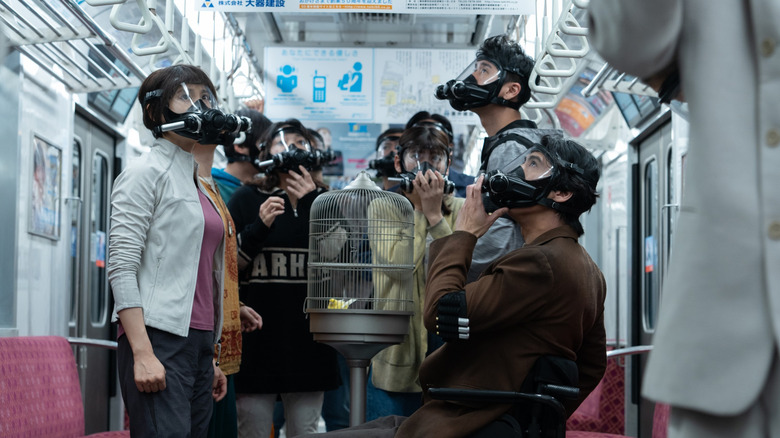 A group of people wearing gas masks cluster a subway car looking upward on Alice in Borderland season 3