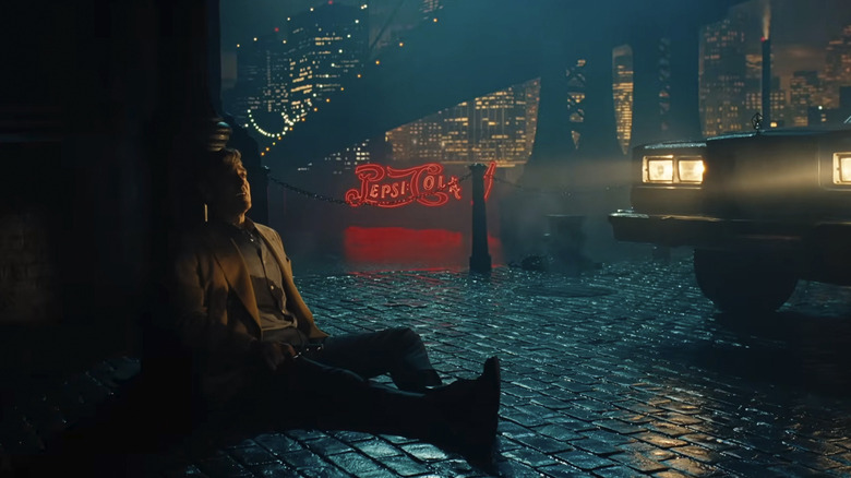 Jay Kelly, playing a movie character, is dying on a slicked brick street with a city in the background in Jay Kelly