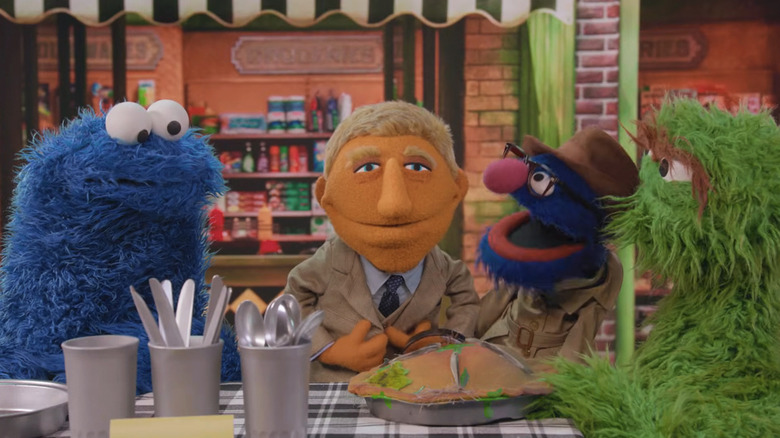 A muppet version of Benoit Blanc stands next to Cookie Monster, Grover, and Oscar the Grouch