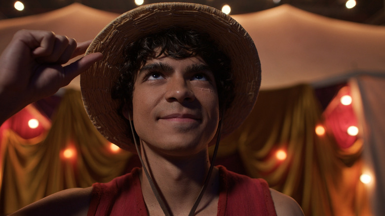Monkey D. Luffy grabs his straw hat and smiles in One Piece