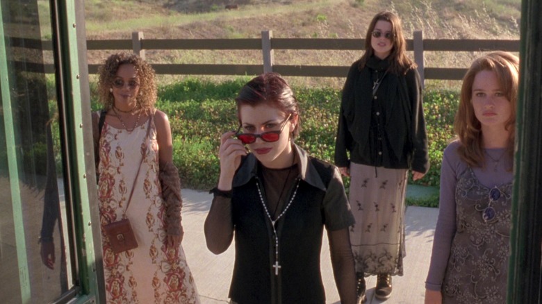 Rachel True as Rochelle Zimmerman, Fairuza Balk as Nancy Downs, Neve Campbell as Bonnie Harper, and Robin Tunney as Sarah Bailey standing around a bus in The Craft