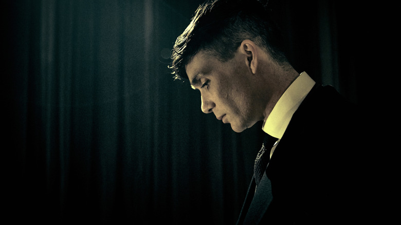 Cillian Murphy as Thomas Shelby looking down in front of a dark background in Peaky Blinders