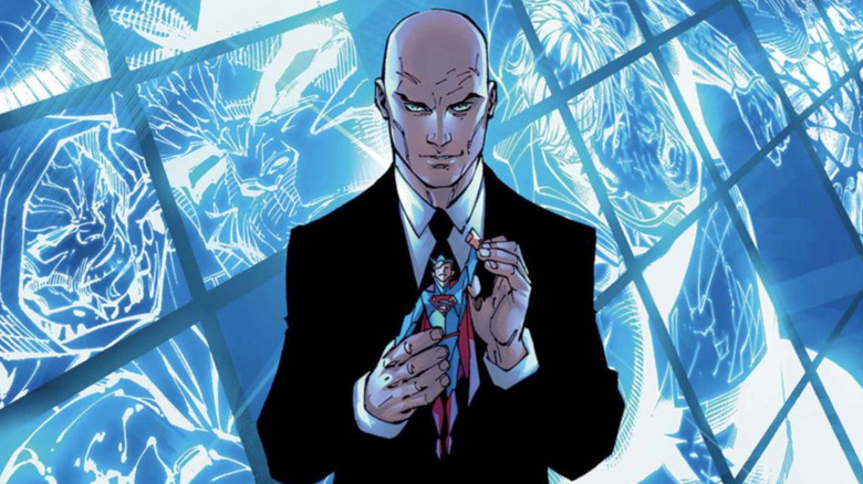 Comic panel of Lex Luthor standing in front of TV screens and holding a Superman doll