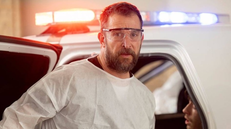 Robby with goggles on in front of a squad car looking worried on The Pitt