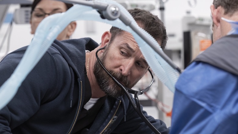Dr. Robby wearing his stethoscope listening with tubes in front of him on The Pitt
