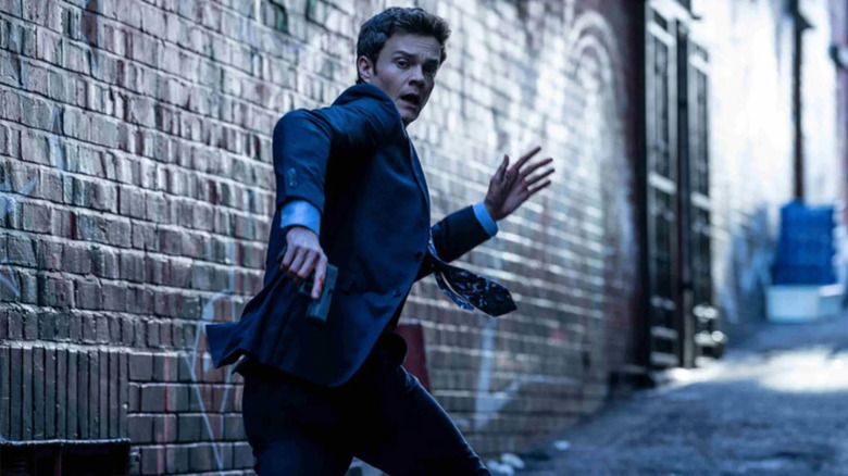 Nathan Caine (Jack Quaid) flees down an alley while holding a gun in Novocaine