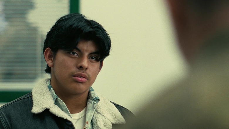 Bluto sits in a dull high school room, being interrogated by Danvers in One Battle After Another