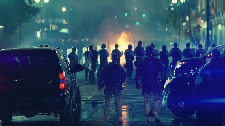 Col. Lockjaw surveys the protest in Baktan Cross with fire raging in the streets in One Battle After Another