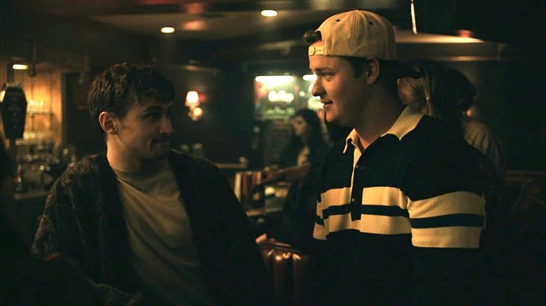 Bear and Ian stand next to each other at a bar in Obsession, looking at each other
