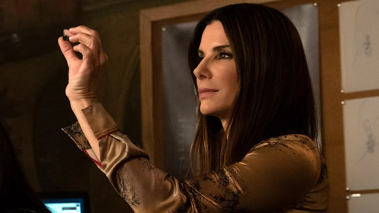 Debbie holding a jewel up to the light and smirking in Ocean's 8