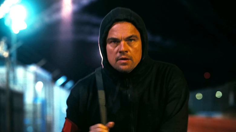 Leonardo DiCaprio as Bob walking away from fireworks with his hoodie on in One Battle After Another