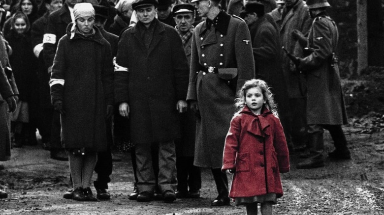 black and white image of people standing in the street with a little girl in a red coat in the foreground