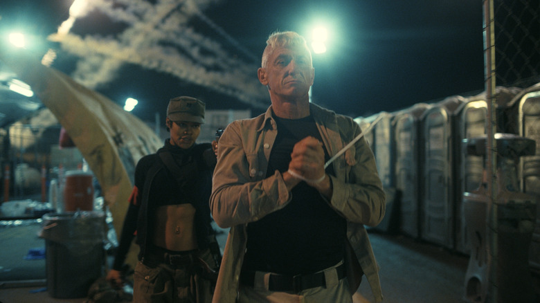 Sean Penn as Lockjaw with his hands bound by a zip tie as Teyana Taylor as Perfidia holds him at gunpoint in One Battle After Another