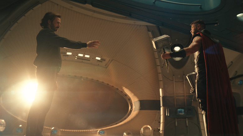 Chris Evans as Steve Rogers extends his arm to Chris Hemsworth as Thor in a spaceship in front of a window in Avengers: Doomsday