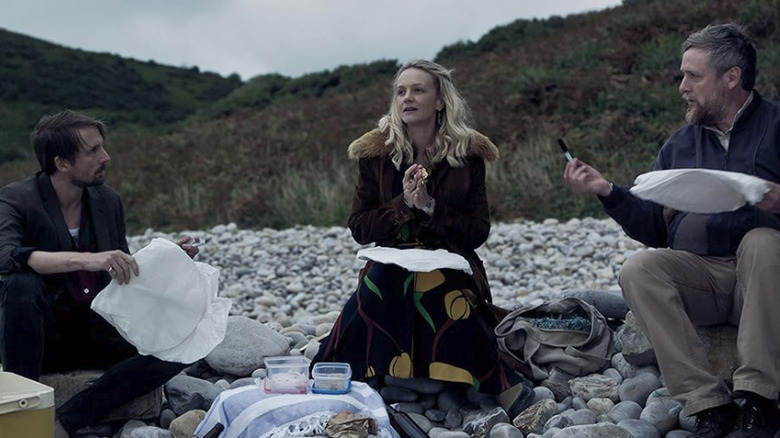 Herb, Nell, and Charles sit on a rocky beach in The Ballad of Wallis Island