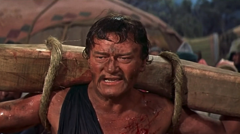 John Wayne's Temujin looks angry with his hands bound to a wooden yoke in The Conqueror