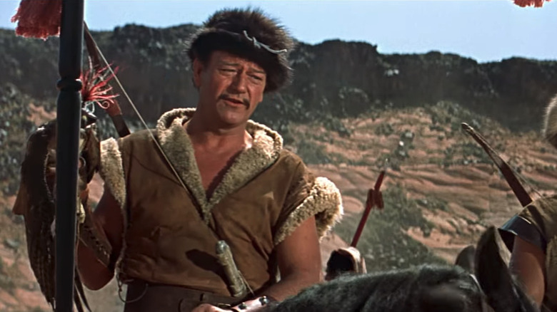 John Wayne's Temujin looks across frame and talks as he sits on a horse in The Conqueror