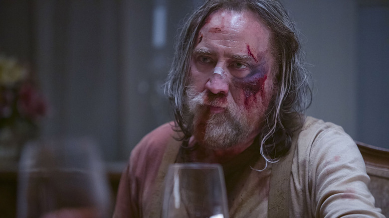 Nicolas Cage as Robin Feld sits with blood and bruises on his face in Pig