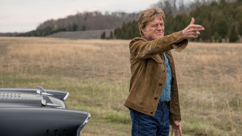 Robert Redford as career criminal Forrest Tucker standing in a field and holding up his hand like a gun in The Old Man & the Gun