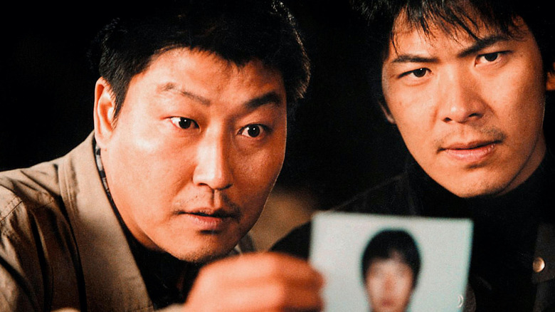 Song Kang-ho as Park Doo-man and Kim Sang-kyung as Seo Tae-yoon hold up a photograph in Memories of Murder