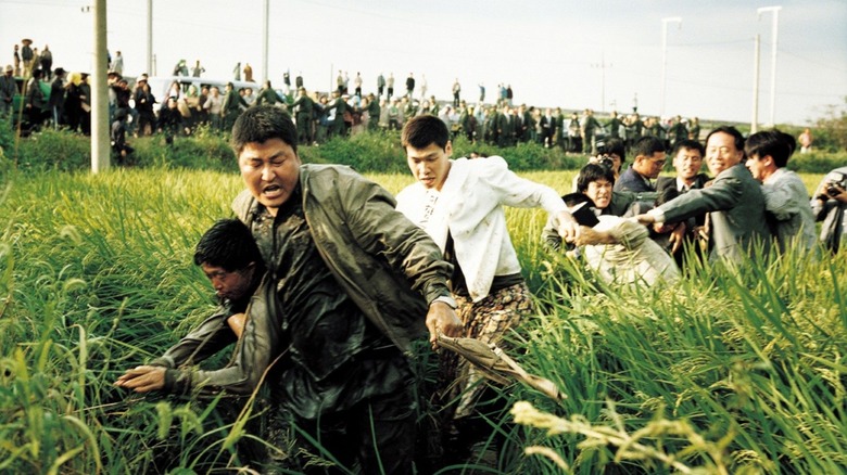 Detective Park carries a suspect through a field as a mob chases behind them in "Memories of Murder"