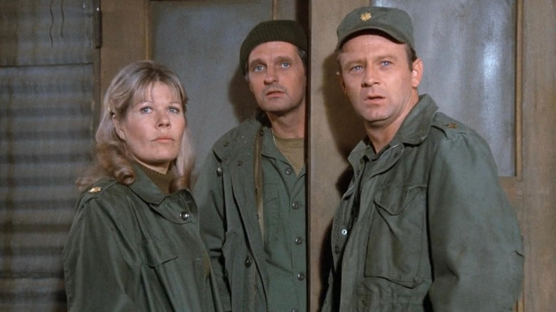 Loretta Swit as Hot Lips, Alan Alda as Hawkeye, and Larry Linville as Franks standing together in M*A*S*H