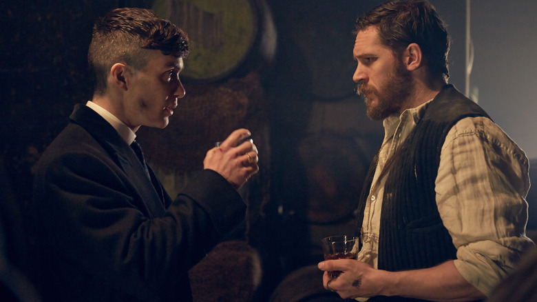 Cillian Murphy as Tommy Shelby having a drink with Tom Hardy as Alfie Solomons in a warehouse in Peaky Blinders